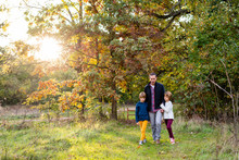 Father Walking With His Two Daughters In A Park During Autumn