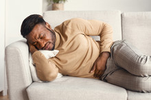 Afro Man Touching Aching Stomach Lying On Couch At Home