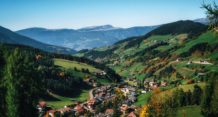 Aerial view of mountain alpine village and green meadows in Italian Dolomites Alps, Funes Valley, Trentino Alto Adige, Italy in autumn