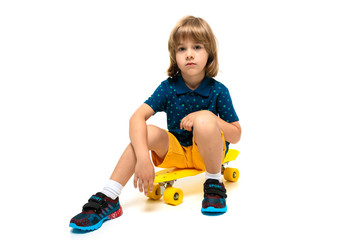 young european cute child in sportswear sitting on a yellow skateboard on a white background