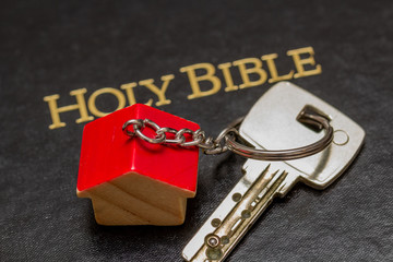 key with wooden house key chain lying on Holy Bible