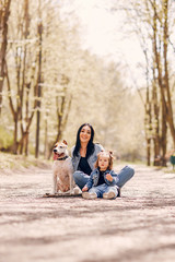 Beautiful mother with daughter. Family in a spring park. Woman in a blue jacket. Family with a cute dog