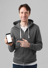 smiling casual style man holding smartphone with blank white screen isolated on gray background