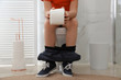 Boy with paper suffering from hemorrhoid on toilet bowl in rest room, closeup