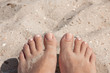 Female feet with natural pedicure nails on beach sand