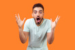 Oh my god, wow! Portrait of amazed brunette man with beard in white t-shirt staring at camera with big eyes and open mouth, absolutely shocked by news. indoor studio shot isolated on orange background