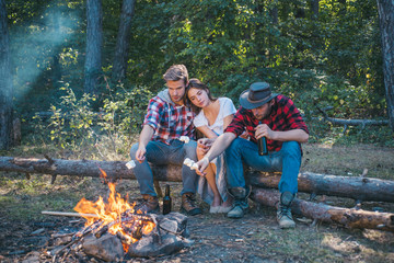 Roasting marshmallows barbecue. Friends camping in forest. Picnic friends. Happy friends on a camping trip relaxing by campfire. Hikers sharing impression of walk and eating.