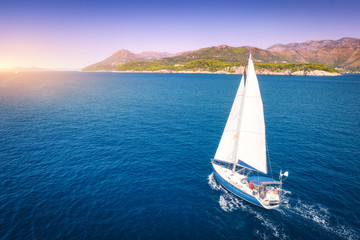 Wall Mural - Aerial view of beautiful white sailboat in blue sea at bright sunny summer evening. Adriatic sea in Croatia. Landscape with yacht, mountains, transparent blue water, sky at sunset. Top view of boat