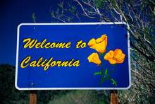 This Is A Road Sign That Says, Welcome To California. It Has The State Flower On It, The Poppy. The Sign Is Against A Blue Sky.