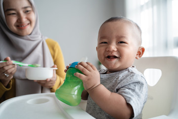 cute asian baby boy smiling to camera while eating sitting on high chair