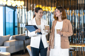 Wall Mural - Two asian businesswomen talking during coffee break in modern office or coworking space, coffee break, relaxing and talking after working time, business and people partnership concept