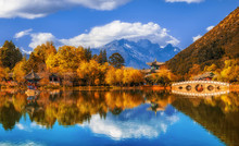 Panorama Landscape View Of The Black Dragon Pool At Jade Spring Park With Marble Bridge Over The Jade Dragon Mountain Under Blue Sky, Lijiang, Yunnan Province, China. China Culture And Travel Concept