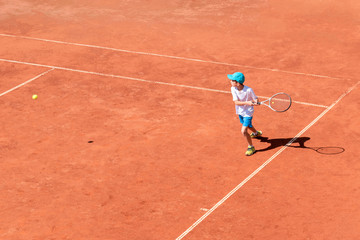 Wall Mural - Boy tennis player plays on clay tennis court. The child is trying to hit the backhand, focused on the ball. Sports action frame. Active games. Copy space.