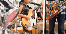 Beautiful, Talented Young Asian Girl Sings And Plays Natural Wood Color Electric Bass Guitar On Contest Stage With Passion, Joy And Confidence. Indy Family Perform, Father On Guitar, Brother On Drums.