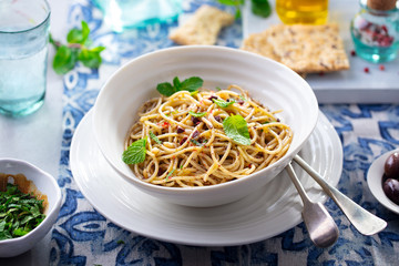 Spaghetti pasta with olives, fresh herbs sauce in a white bowl. Blue textile background.