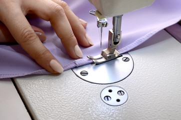 Seamstress sews fabric on a sewing machine closeup. Lilac fabric for tailoring dresses. Small business concept.