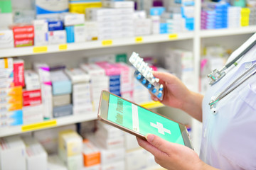 Doctor holding medicine capsule pack and computer tablet for filling prescription in pharmacy drugstore.