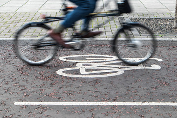 Painted cycle path bicycle sign on the ground with a rider passing.  Motion blurr on the bike and rider.