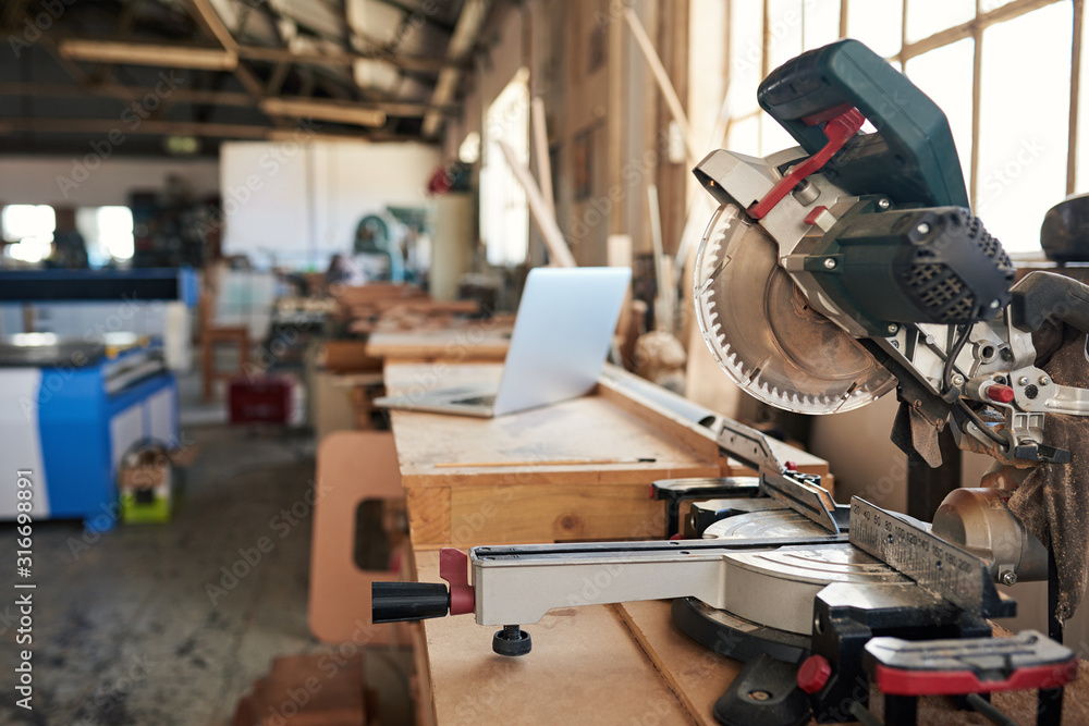 Mitre saw and laptop on workbenches in a woodworking shop - obrazy, fototapety, plakaty 