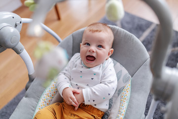 adorable caucasian 6 months old baby boy sitting in his rocker chair, talking baby language and look