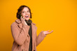 Photo of funny cheerful pretty lady hold telephone speaking friends sharing fresh news wear casual modern style pink coat warm green knitted pullover isolated yellow color background