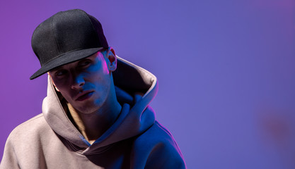 Wall Mural - Men portrait in a neon light. Beneath in the hoodie and hat. Dark face. Hip-hop style.