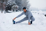 Fototapeta Panele - Young man stretching legs on snowy day in the city