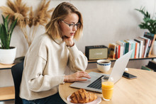 Photo of caucasian woman using laptop while having breakfast at home