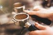 Barista woman holding coffee holder with ground coffee near professional coffee machine close up
