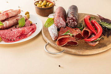 Wall Mural - delicious meat platters served with olives, spices on plate and wooden board on beige background
