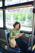 © makistock - Beautiful happy young woman sitting in city bus, looking at mobile phone