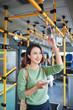 © makistock - Young adorable joyful woman is standing on the bus using the phone and smiling.
