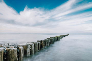 Wall Mural - stony beach with old wooden Pier at the baltic sea on a beautiful day with blue sky - long exposure 