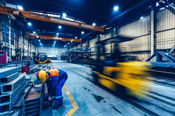 Factory work. Forklift moving and a worker taking a steel profile