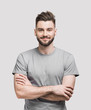 canvas print picture - Portrait of handsome smiling young man with folded arms. Smiling joyful cheerful men with crossed hands studio shot. Isolated on gray background
