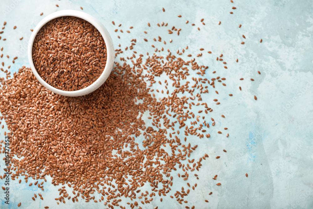 Bowl with flax seeds on color background