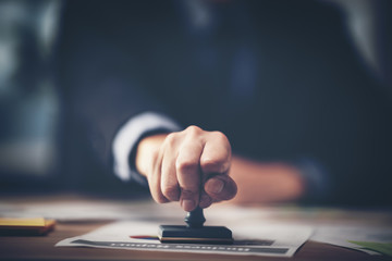 Wall Mural - Close-up of a person's hand stamping with approved stamp on certificate document public paper at desk, notary or business people work from home, isolated for coronavirus COVID-19 protection	