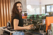© studioprodakshn - smiling barista woman preparing coffee for client standing with coffee holder full of coffee beans near professional coffee machine, barist work routine