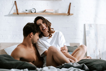 Wall Mural - muscular man smiling near happy girlfriend in bedroom