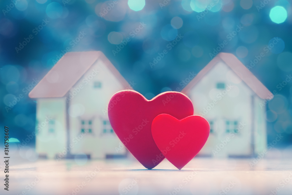 Two hearts and house models over defocused lights. Valentine's day concept - obrazy, fototapety, plakaty 