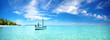 canvas print picture - Boat in turquoise ocean water against blue sky with white clouds and tropical island. Natural landscape for summer vacation, panoramic view.