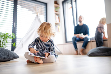 Cute small toddler girl indoors in bedroom playing with tablet.