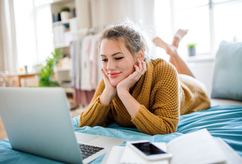 Young woman with laptop lying on bed indoors at home, relaxing.