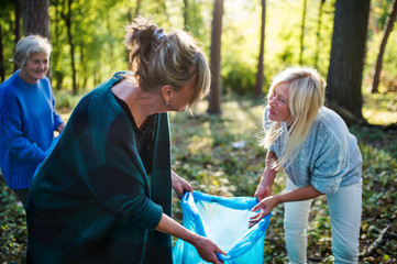 Wall Mural - Senior women friends picking up litter outdoors in forest, a plogging concept.