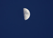 View Of The Half Moon And Its Craters Over A Dark Blue Sky