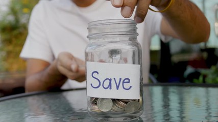 Wall Mural - man putting the coin into a clear glass jar ,saving money concept