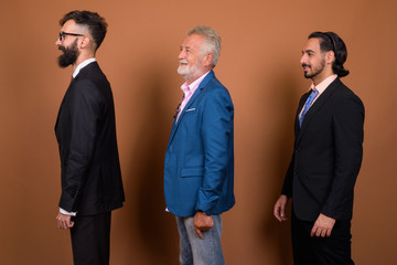 Wall Mural - Three multi ethnic bearded businessmen together against brown background