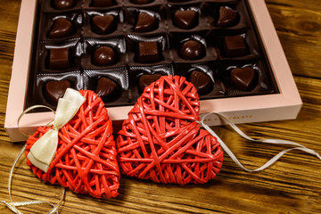 Wall Mural - Assorted chocolate candies in a box and two red hearts on wooden table. Valentine Day concept