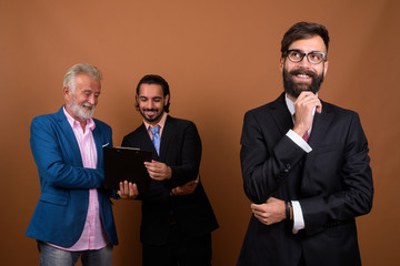 Wall Mural - Three multi ethnic bearded businessmen together against brown background