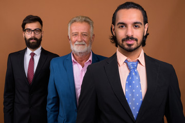 Wall Mural - Three multi ethnic bearded businessmen together against brown background